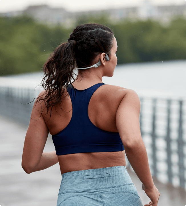 Une coureuse portant un casque de sport à conduction osseuse OpenRun gris de Shokz. Toute la liberté des oreilles.