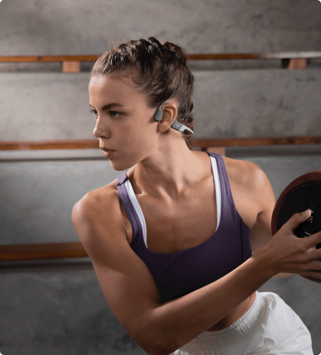 Une femme sportive portant un casque de sport à conduction osseuse OpenRun gris de Shokz. Toute la stabilité pour le sport.