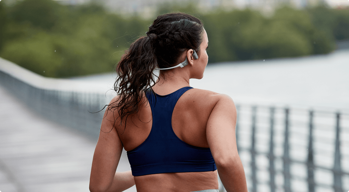 Une coureuse portant un casque de sport à conduction osseuse OpenRun gris de Shokz. Toute la liberté des oreilles.